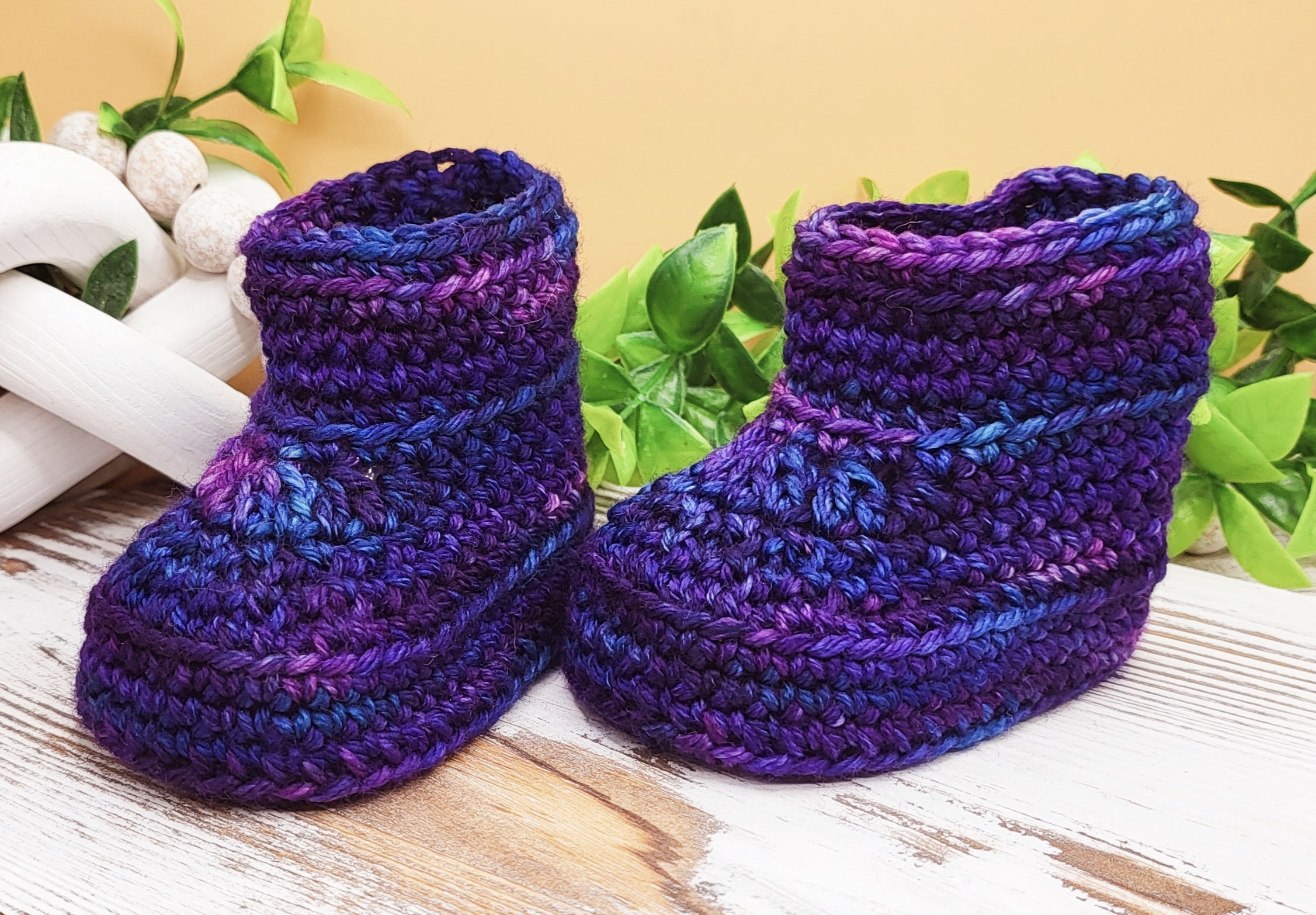 Purple and blue Alex Baby Booties with raised cuff edging, shown as a finished example of the crochet pattern.