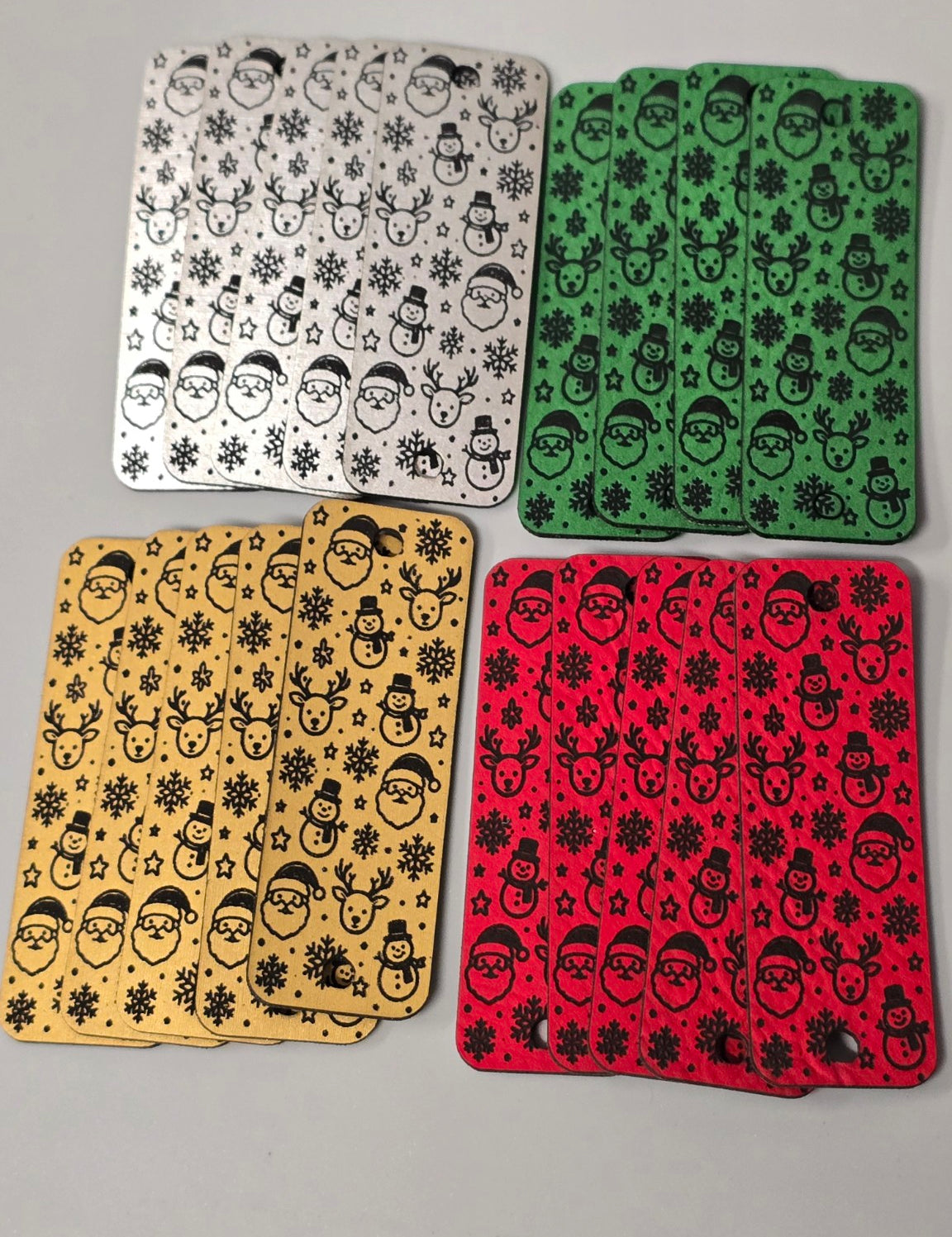 Set of 20 Christmas faux leather fold-over tags in silver, green, gold, and red, engraved in black with Santa faces, snowmen, reindeer, and snowflakes.