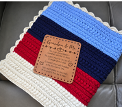 Illustrative mockup of Grandma & Me patch resting on a red navy blue and cream crochet blanket